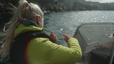 Una-Chica-Guapa-Pescando-En-Un-Pequeño-Barco-A-Motor-En-Un-Hermoso-Fiordo-En-El-Sur-De-Noruega,-Pesca-Amateur,-Chica-Con-Chaleco-Salvavidas