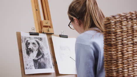 artista adolescente sentada en un caballete dibujando una imagen de un perro de una fotografía en carbón