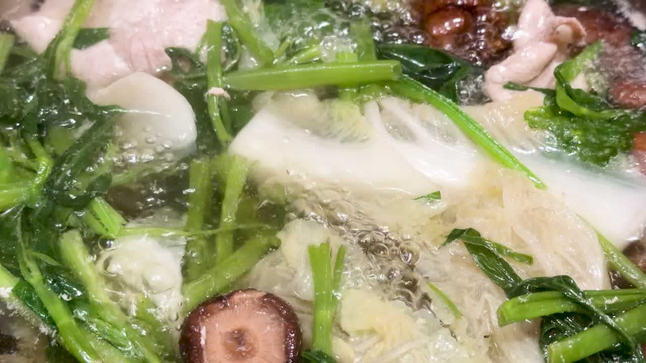 Fresh meat, mushrooms, and vegetables boil in clear broth under bright lighting, close-up perspective