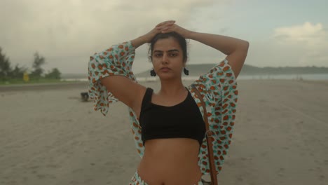 in this medium shot, we see an indian woman wearing vibrant red floral clothing as she stands gracefully at the beach