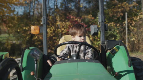 asian kid playing behind the wheel of an old tractor on a farm. front view