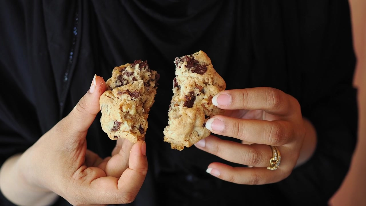 Woman Holding and Breaking a Chocolate Chip Cookie