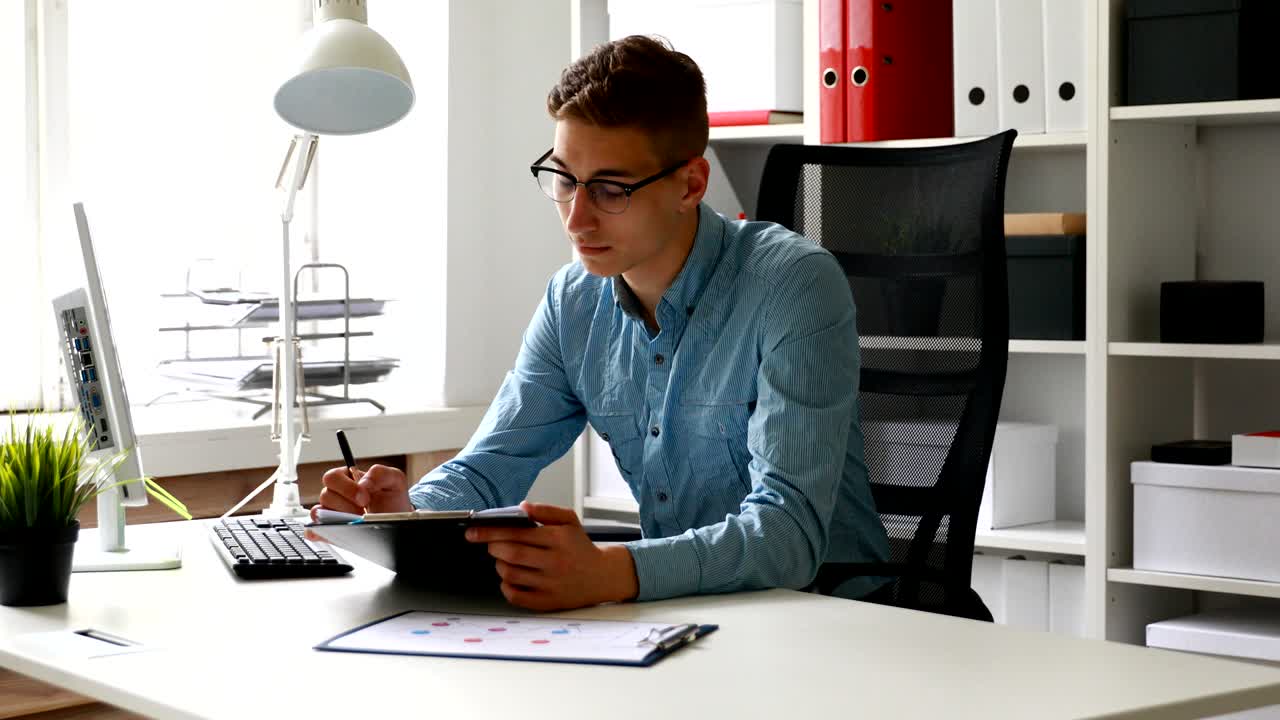 hombre de negocios con gafas, sentado en la mesa y mirando a la cámara
