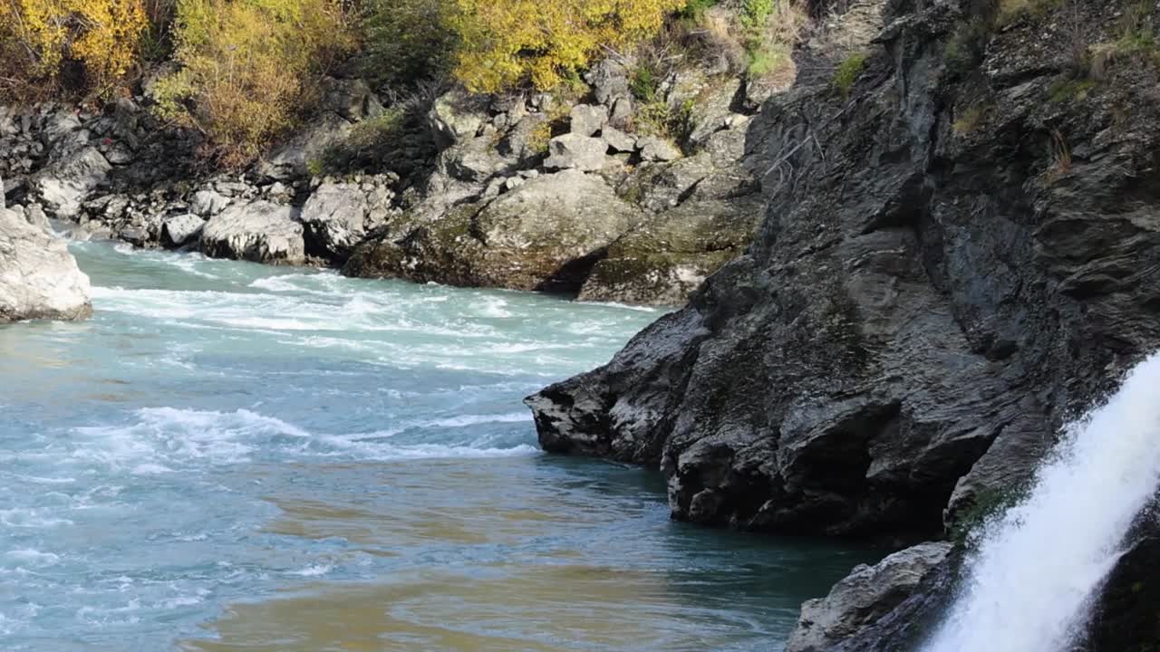 Cascate impetuose di acqua bianca si riversano in un fiume turchese circondato da scogliere frastagliate e alberi autunnali