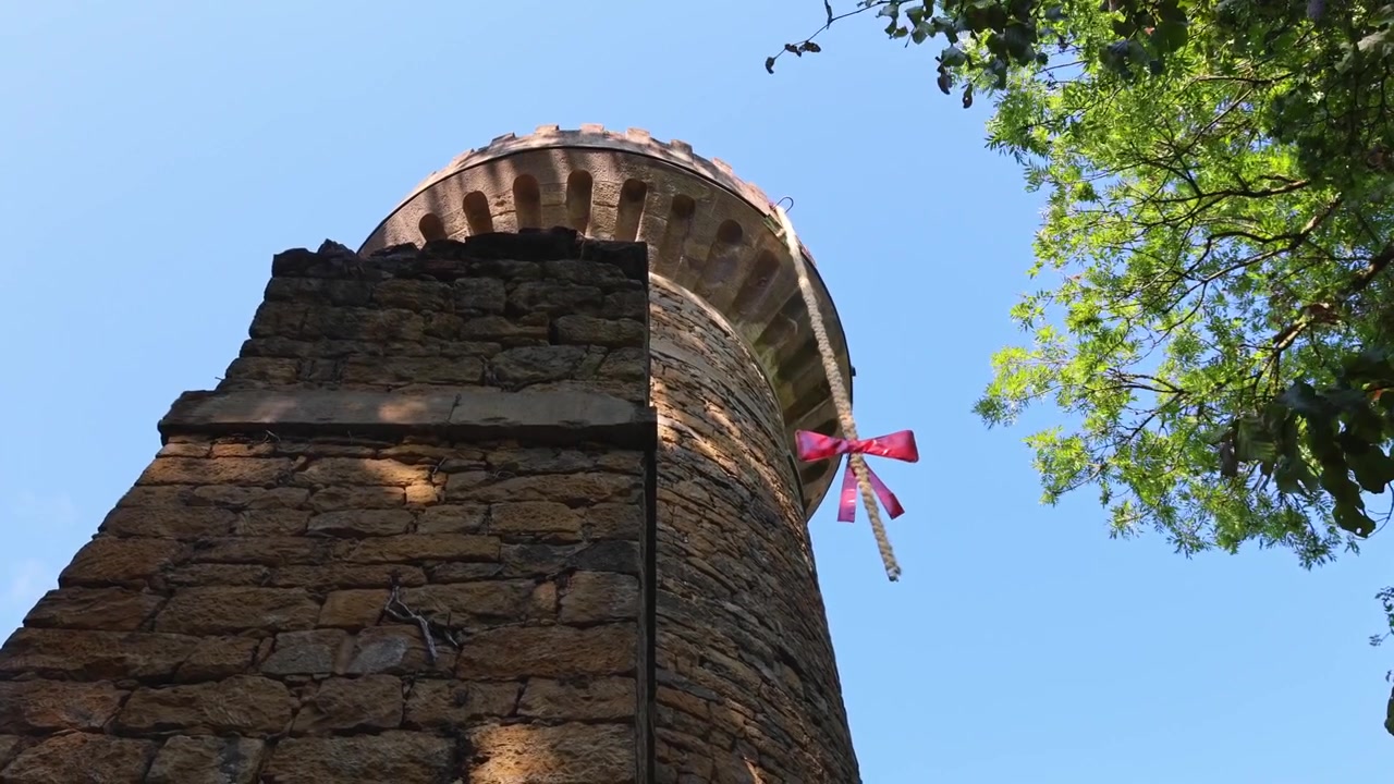 Torre storica in pietra si erge sopra il verde circostante contro un cielo azzurro limpido