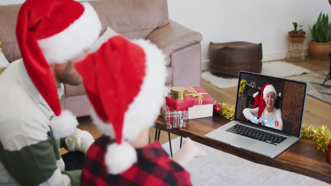 padre y hijo caucásicos usando sombreros de santa en una videochat portátil durante la navidad en casa