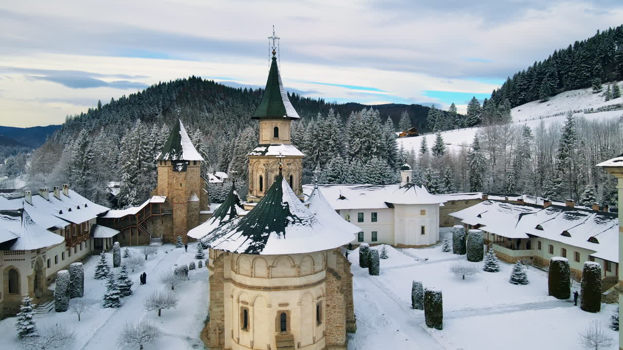 Lotniczy widok z drona na monastyr Putna zimą, Rumunia. Wewnętrzny dziedziniec z przechadzającymi się turystami, nagie drzewa, śnieg, wzgórza wokół
