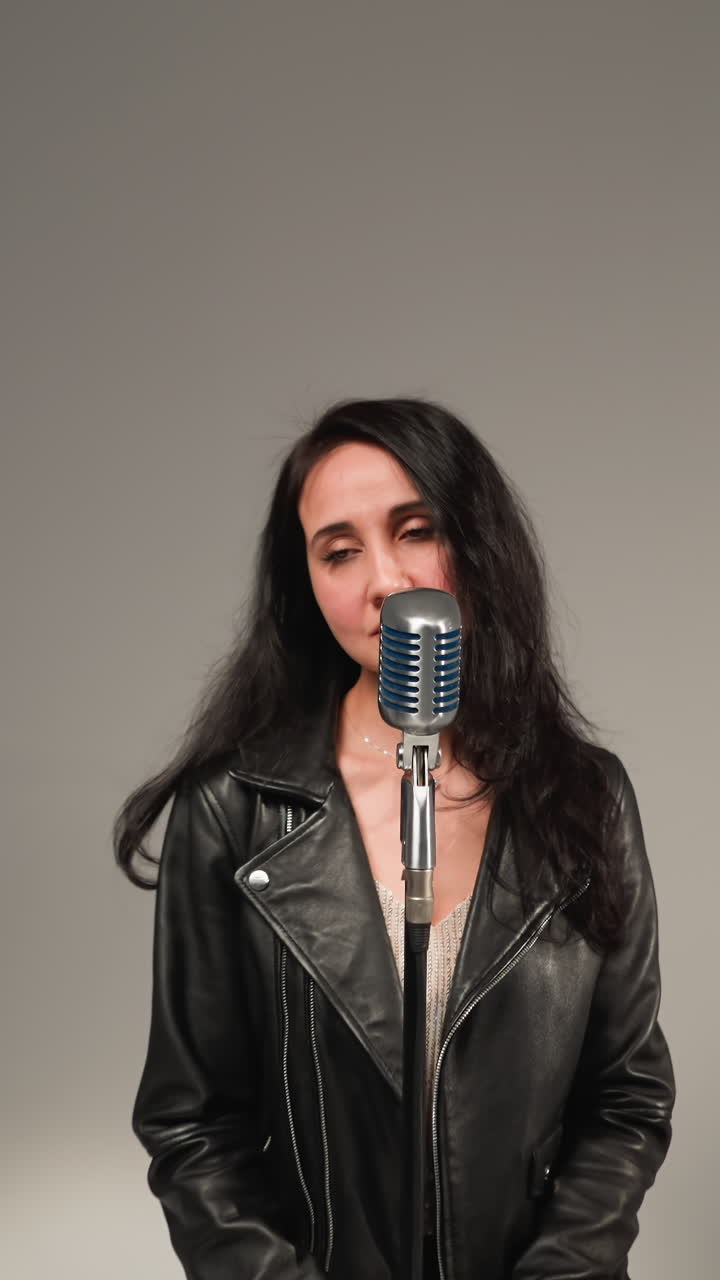 A beautiful vocalist in a black leather jacket,smiling and singing with eyes closed,stands at a vintage microphone on a high stool. A guitarist plays a red guitar and a keyboardist works a red sampler