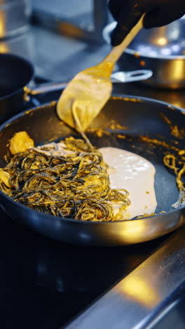cooking some pasta on the frying pan with sauce. some cream is poured into dish and stirred with spatula. vertical video.