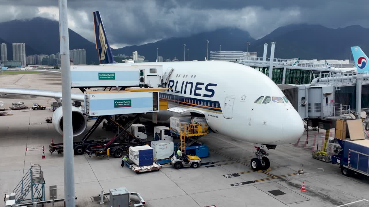Aircraft ground crew managing logistics and cargo operations for an Airbus A380 at Hong Kong International Airport. Busy airport scene with workers and equipment.