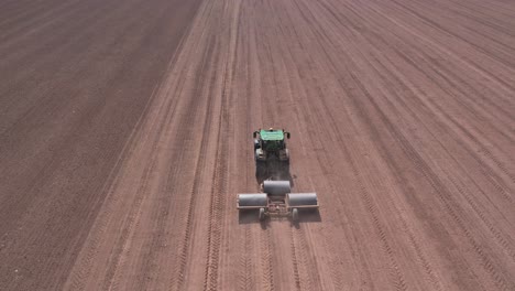 birds's aerial view of tractor flattening land using heavy rollers, large field