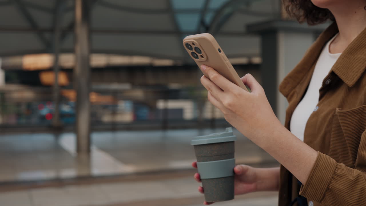 여성이 드폰을 사용하고 야외에서 커피를 마시고 있습니다.