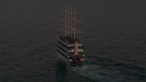 aerial view following multi level tourist sailing ship with masts departing across sunset mediterranean sea