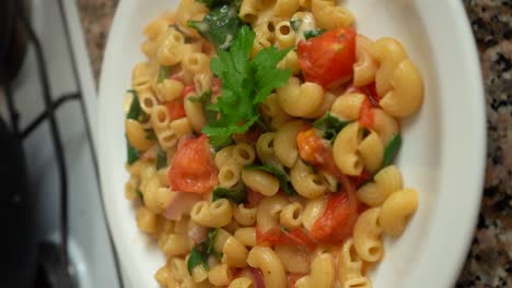 a cook garnish macaroni pasta with cilantro leaves