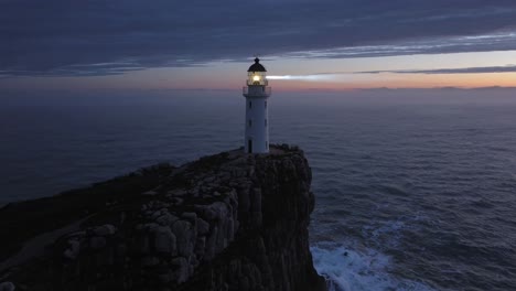 aerial video of a lighthouse on a rocky cliff at dusk, capturing the serene ocean horizon