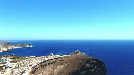 aerial 4k blue sea and sky top view over village cliffside of akra mavro vouno with sailboats docked in distance in santorini greece