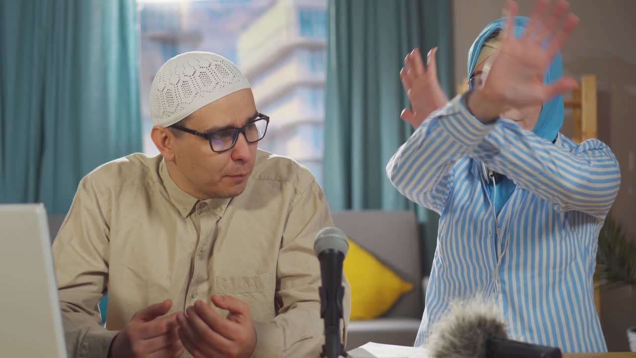 국립 헤드 스카프를 입은 젊은 무슬림 여성, 무슬림 남성이 거실에서 마이크 앞에 앉아 인터뷰 캐스트를 녹음합니다.