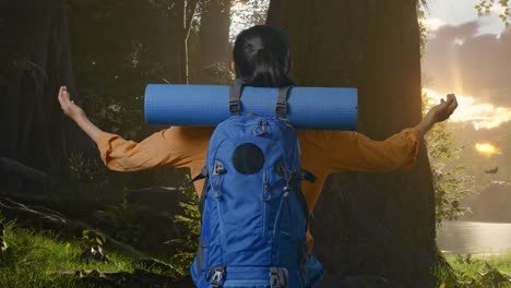 back view of a female hiker with mountaineering backpack spreading arms and looking the view around while exploring forest nature