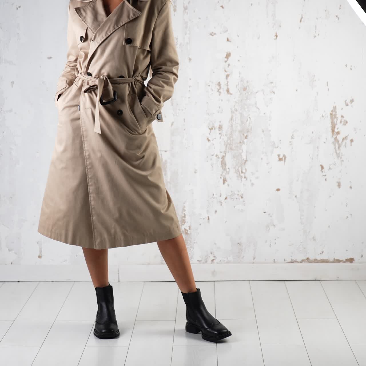 Female wearing beige coat and black boots walks in studio. Fashion and style concept. White wall backdrop