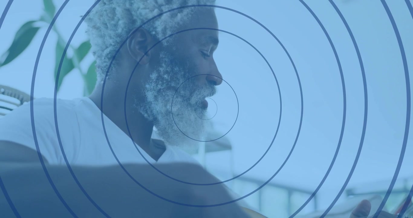 Un homme âgé assis levant son smartphone, balayant l'écran et écoutant avec des écouteurs pour l'usage technologique.