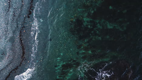 Shallow-calm-waves-crash-on-grey-pebble-beach-shore-in-Newport,-drone-top-down