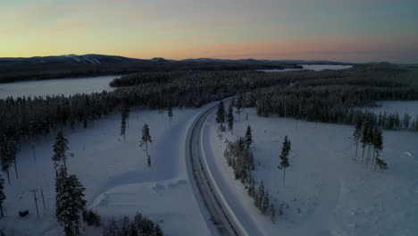 vista aérea sobre una larga y curva carretera helada y nevada entre el paisaje forestal invernal de laponia al amanecer