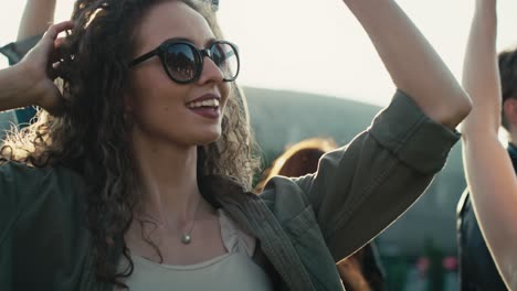 smiling young caucasian woman with curly hair dancing at music festival among friends.