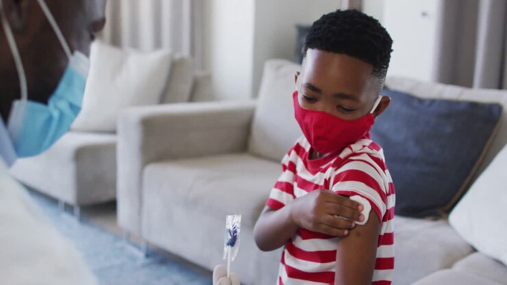 African american doctor wearing face mask gicing a lollipop to a boy after his vaccination at home