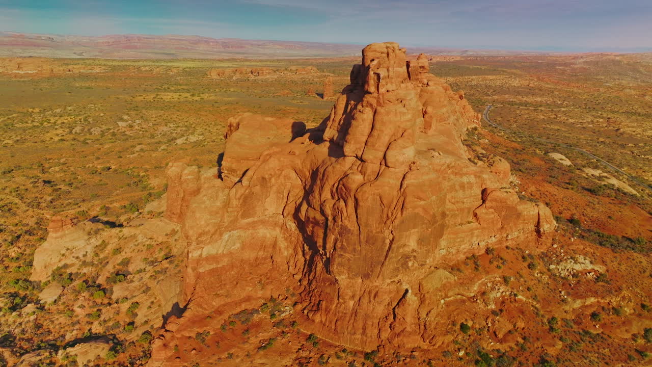 Bright sun lighting the orange mountain. Drone footage around the rock in the deserted landscape. Blue sky at backdrop.