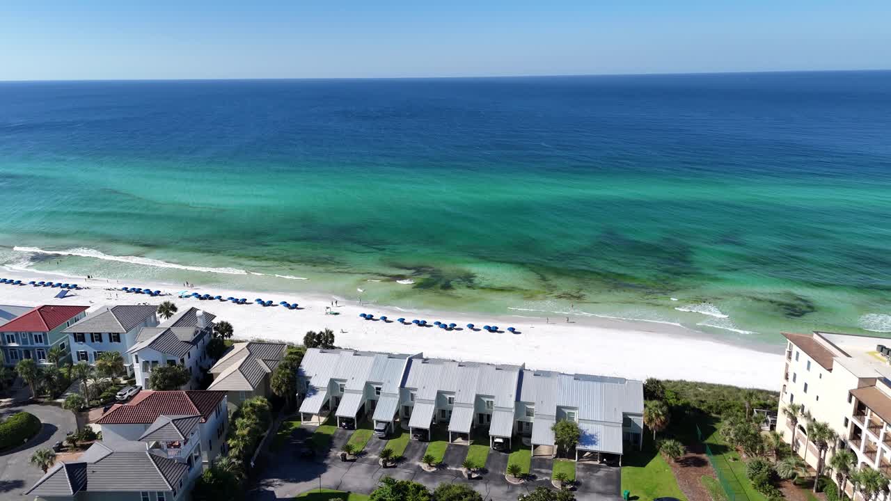 Aerial fly over the coastal settlement with apartments and turquoise ocean along white sandy beach, 30A, Florida, USA