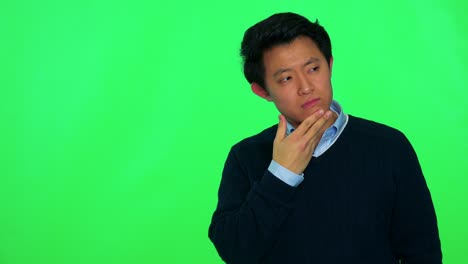 a young asian man rubs his chin thinking about something - green screen studio