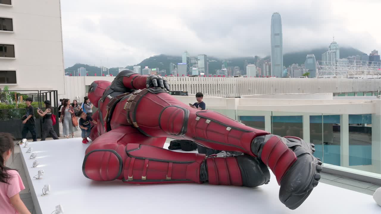 Children play on a massive 8-meter Deadpool display in Hong Kong, while excited onlookers take pictures. The installation promotes Disney's "Deadpool and Wolverine" film