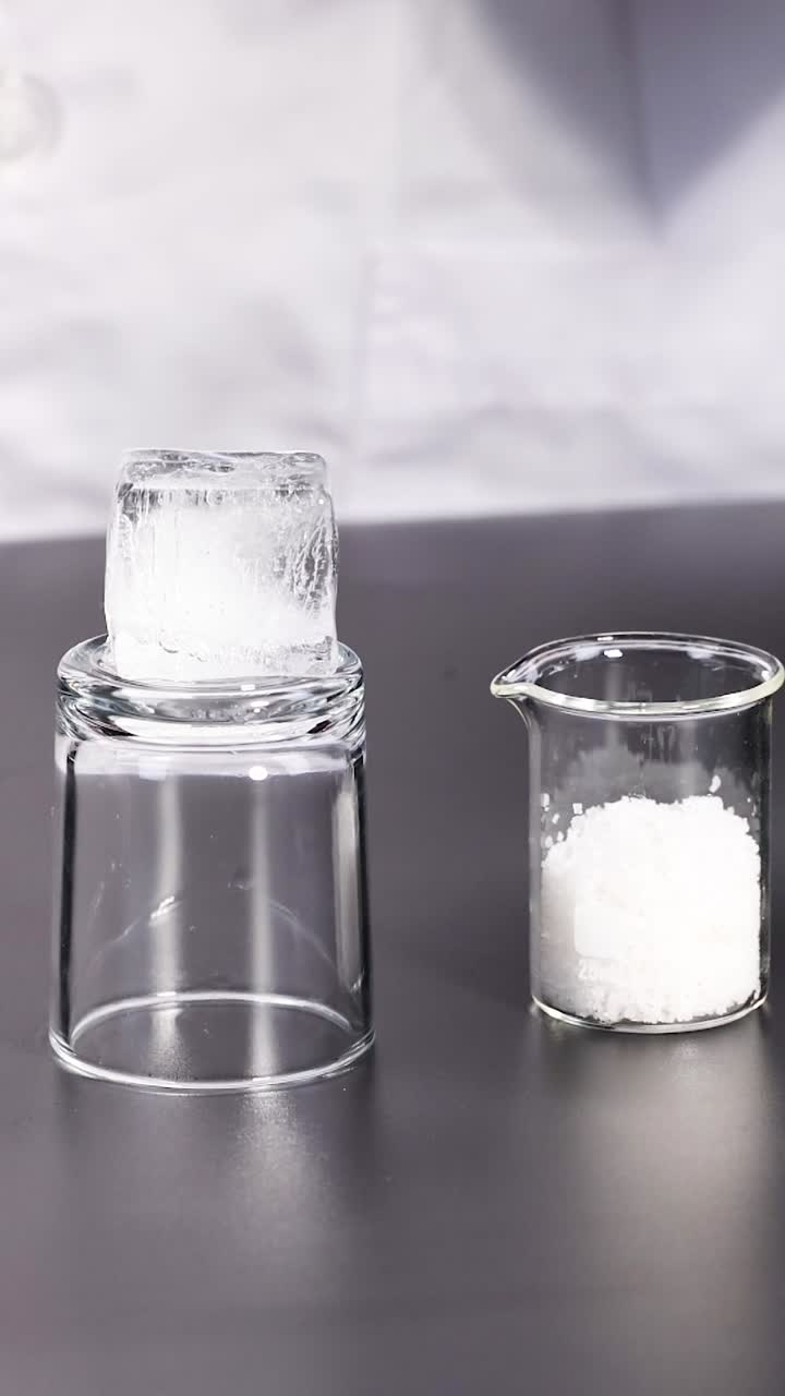 Scienziato in camice da laboratorio dimostra un esperimento sul punto di congelamento di ghiaccio e sale su un tavolo