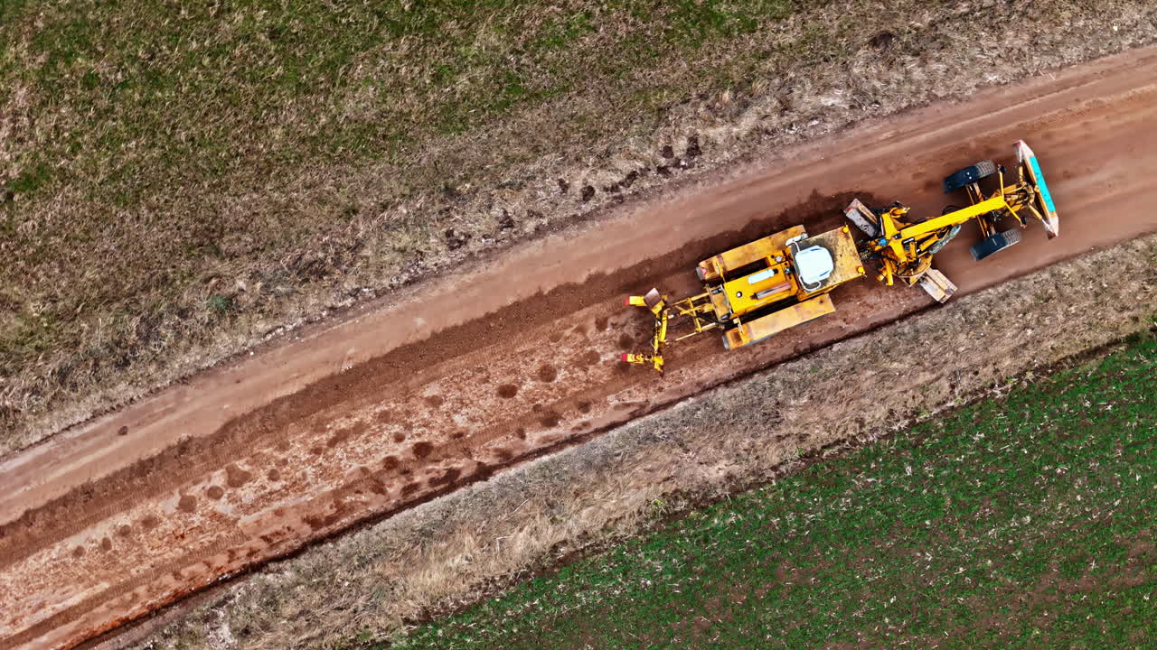 Top view of an excavator leveling a new dirt road between fields
