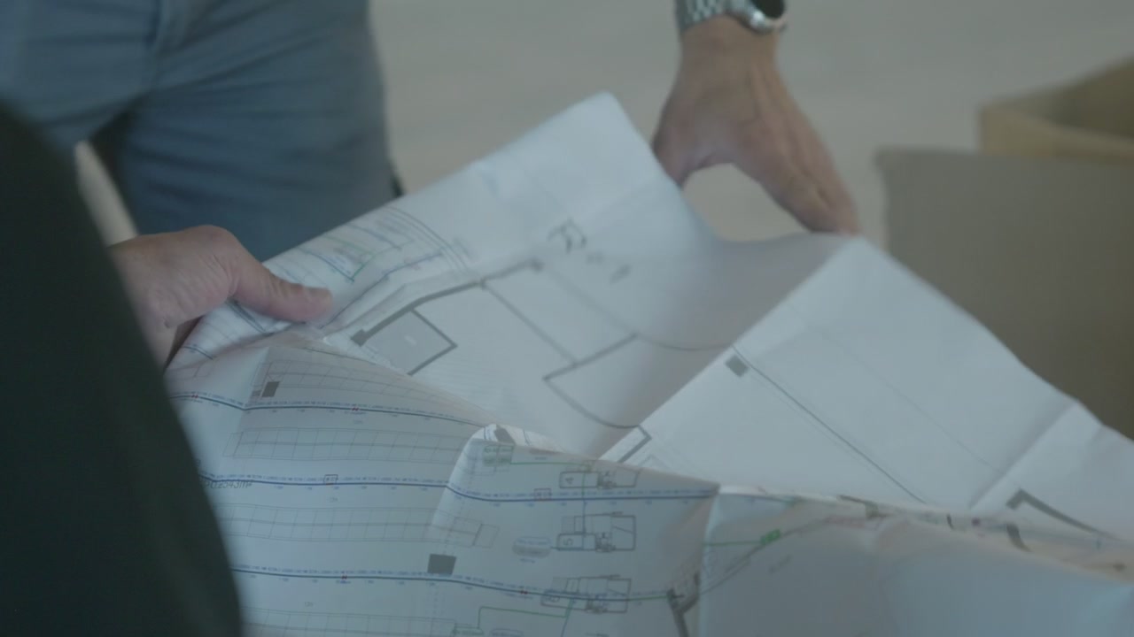 Una persona esamina planimetrie dettagliate per un progetto di costruzione all'interno, con luce naturale soffusa.
