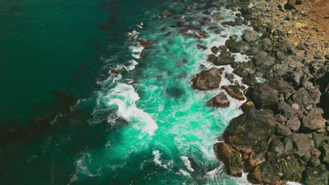 turquoise water splashing by the stones at the shore. rocky coastline of california with white waves splashing by.
