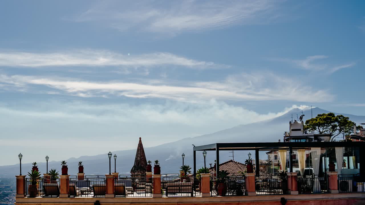 Rooftop terrace in Taormina with a clear view to Mount Etna. Timelapse video with smoke coming out of a volcano summit in a sunny summer day.