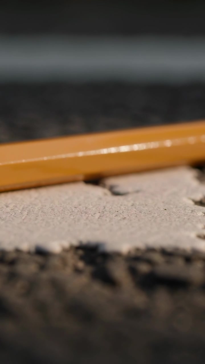Vertical video: Moving camera causing focus shift over yellow glossy pencil on light patch at table