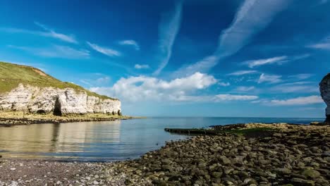 time lapse of a beach in the day time while sun is shining and clouds are moving in the blue sky while cliffs and sea is visible in 4k resolution