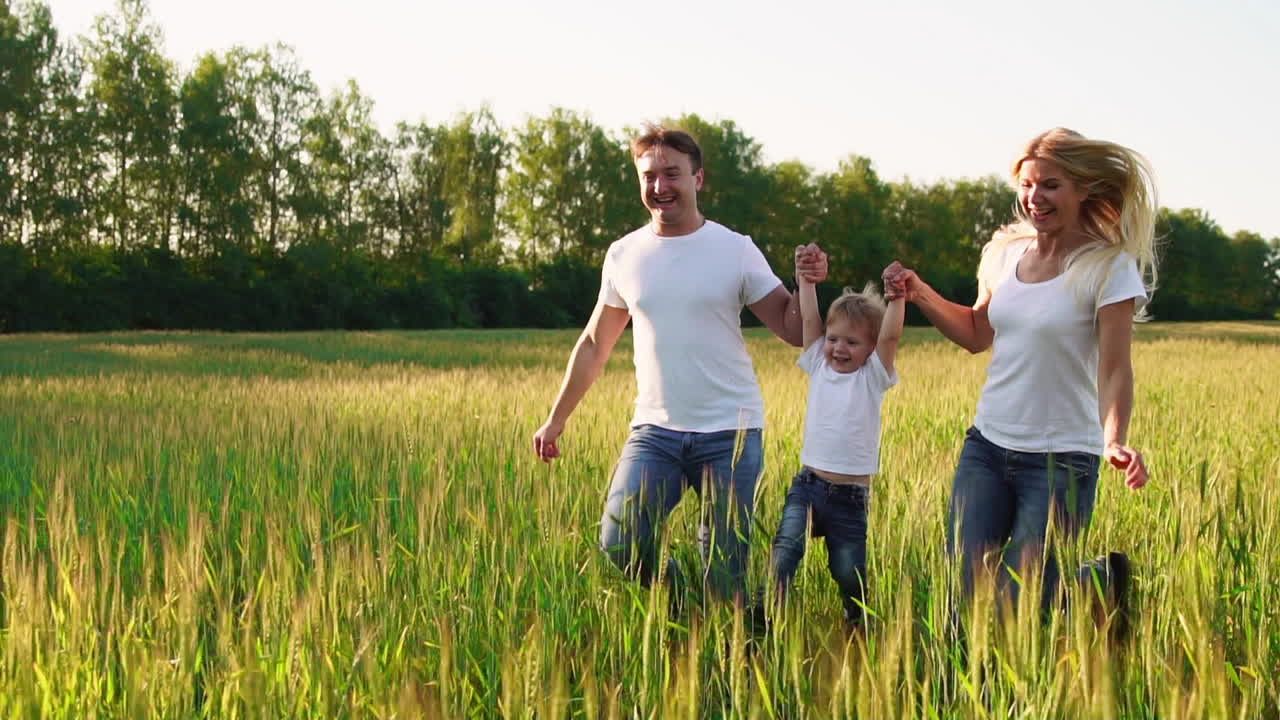 familia feliz: padre, madre e hijo, corriendo en el campo vestidos con camisetas blancas