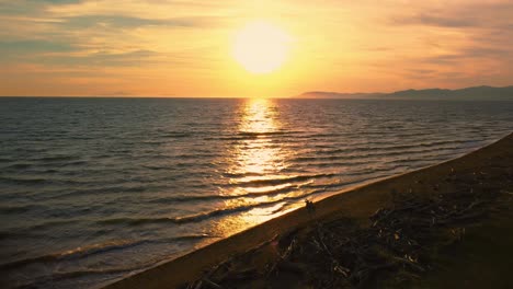 cinematic backwards aerial drone footage of the sunset at a sandy beach at the seaside near alberese in the iconic maremma nature park in tuscany, italy, with waves, islands and a dramatic red sky