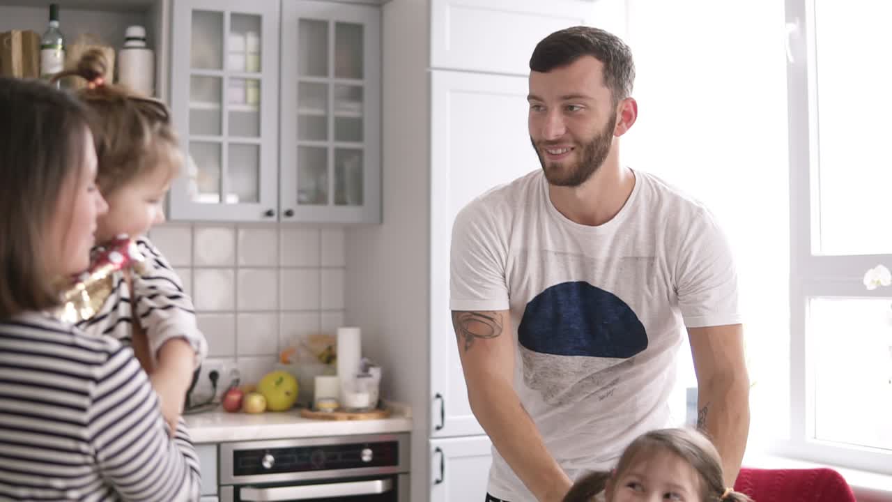 madre sostiene a una hija pequeña en sus brazos, otra hija se queda con papá y sonríe