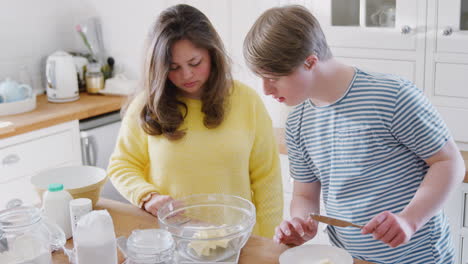 Junges-Down-Syndrom-Paar-Fügt-Butter-Zum-Kuchenrezept-Hinzu,-Das-Sie-Zu-Hause-In-Der-Küche-Backen