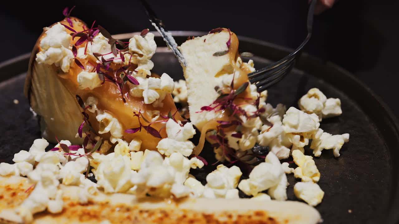 Close up of a woman cutting a cheesecake with a banana split and caramelised popcorn on a black plate at a restaurant