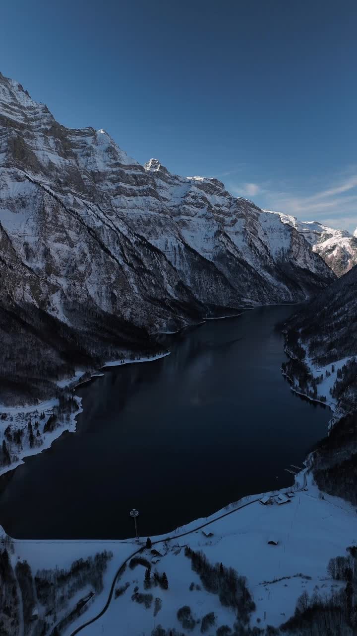 Lago Klöntal, Svizzera alpina invernale: paesaggio naturale innevato con clima freddo, ripresa aerea verticale.
