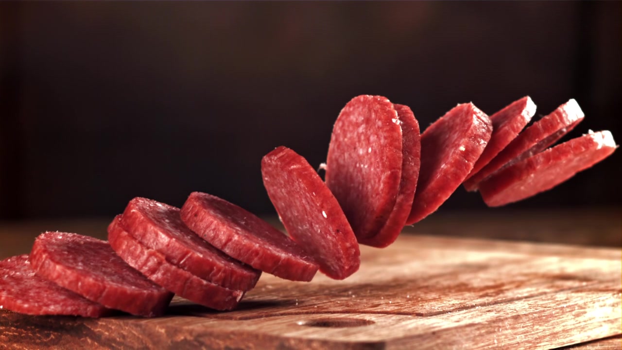 Fette di salame che cadono al rallentatore su un tagliere di legno