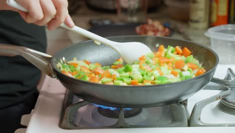 vegetables being stirred in a frypan by caucasian male hand on gas stove