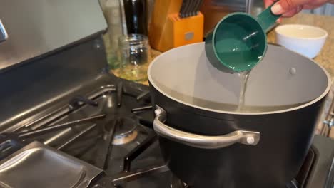 measuring water into a hot pot of boiling water to cook pasta