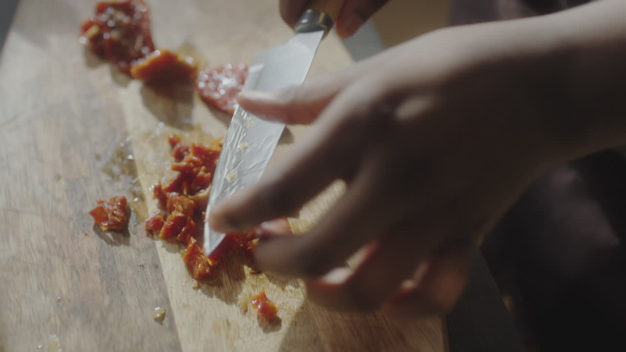 Hands chopping sun-dried tomatoes on a wooden cutting board
