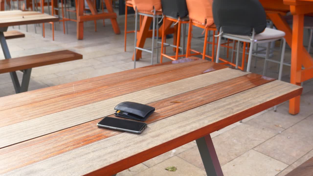 teléfono y billetera en una mesa de madera en un café al aire libre